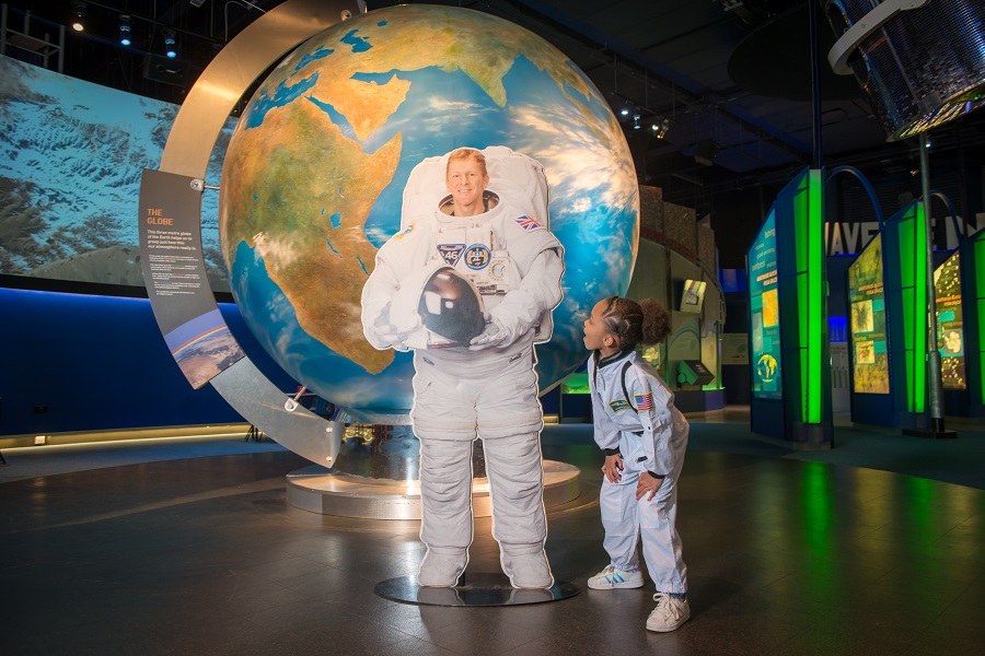 A little girl in a space suit looking up at an astronaut