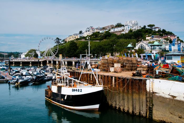 A boat in Torquay Harbour with crab traps, a Ferris wheel, and other boats in the background.