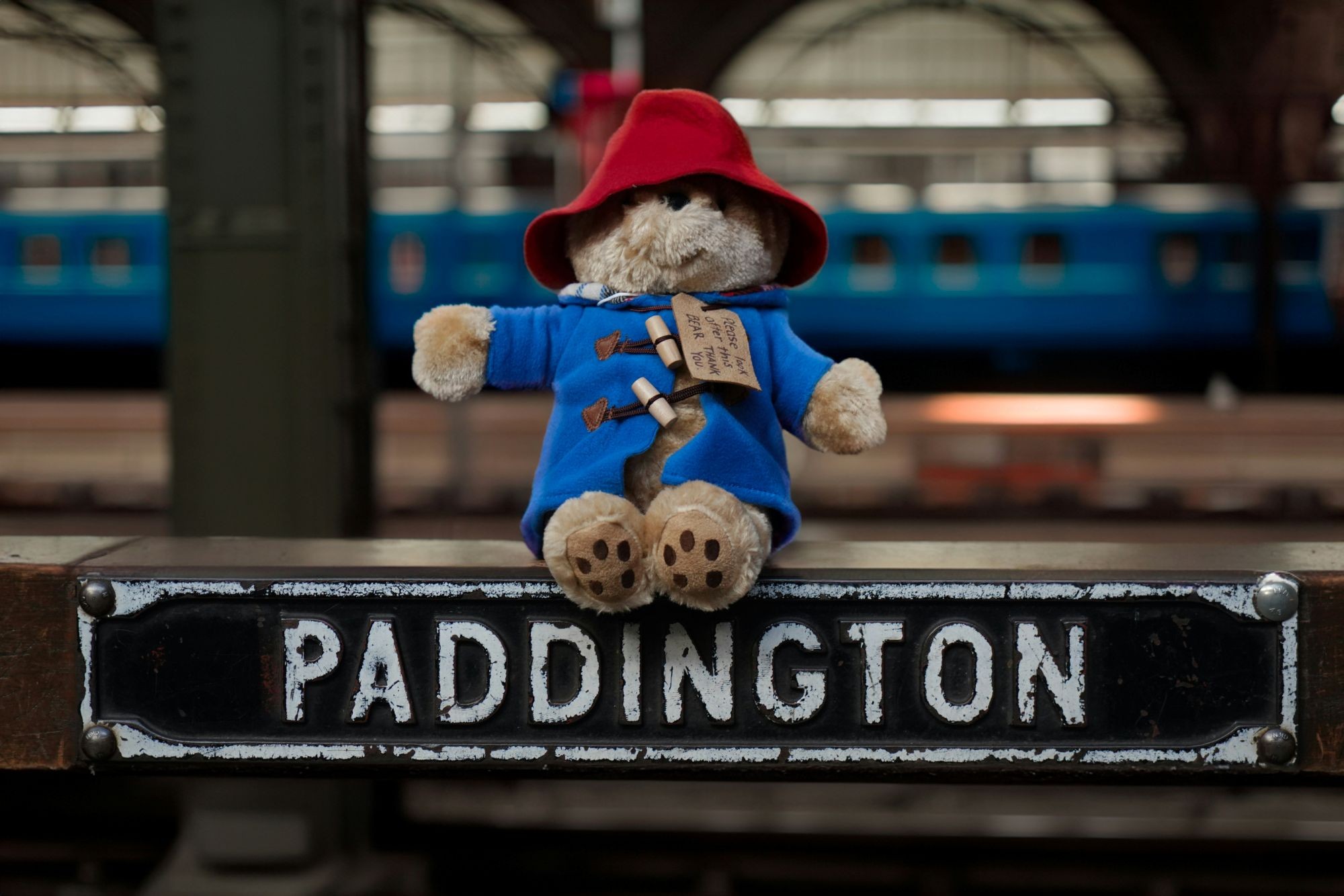A toy Paddington Bear sitting on a small iron sign that says ‘PADDINGTON’