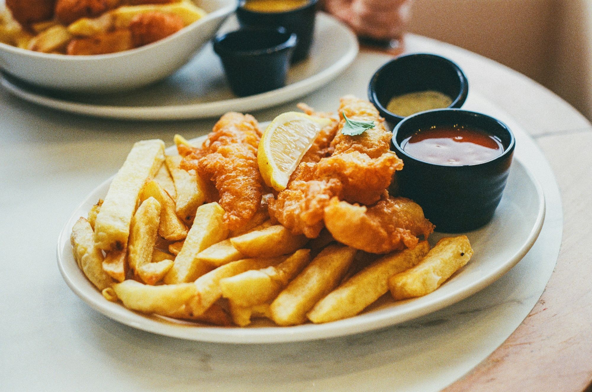 A plate of fish and chips with a lemon and two dips on the side, likely ketchup and tartare sauce.