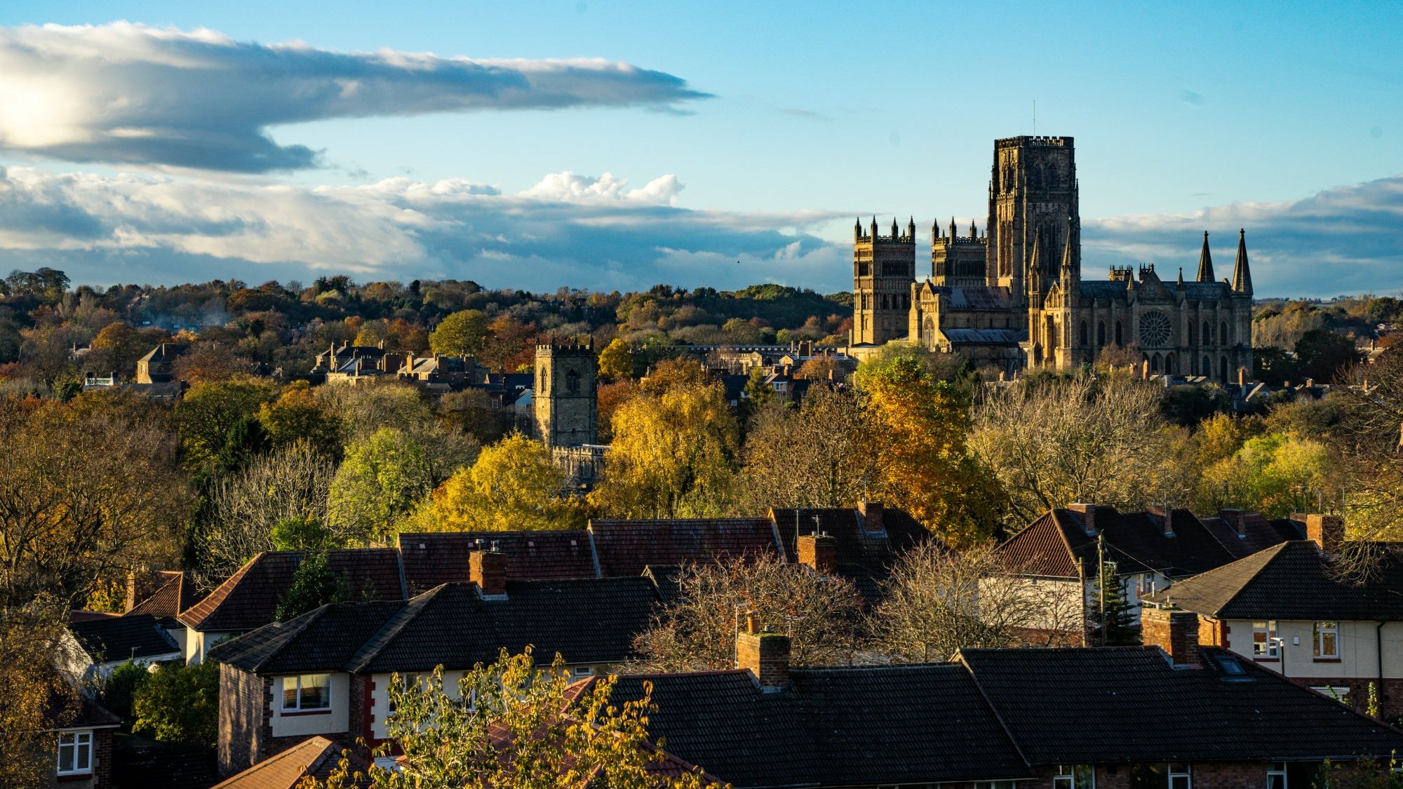 Durham Cathedral towering over residential rooftops and autumn trees.