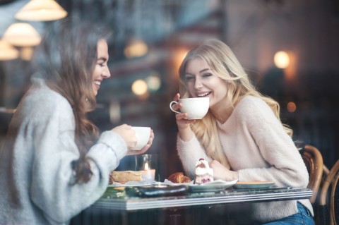 Two laughing women sitting at a table with coffee and cake.