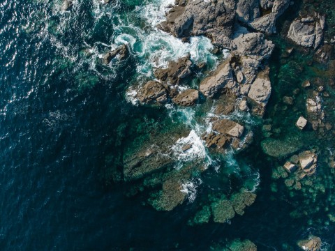 An arial view of a rocky shore with waves crashing against it.