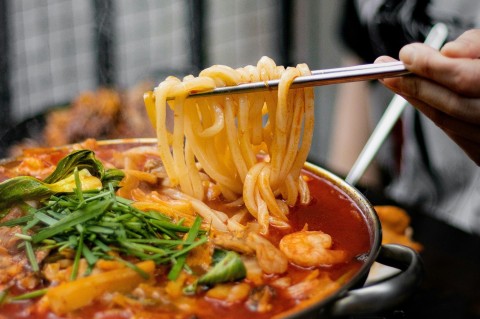 A person holding noodles with chopsticks above a spicy broth.