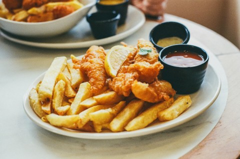 A plate of fish and chips with a lemon and two dips on the side, likely ketchup and tartare sauce.