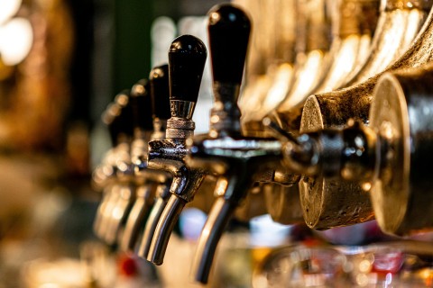 A close-up row of metallic draft beer taps with black handles at a dimly lit bar.
