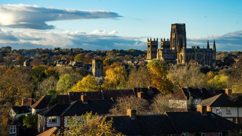 Durham Cathedral towering over residential rooftops and autumn trees.
