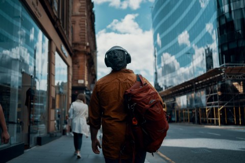 A man with headphones and a backpack walking through Glasgow.