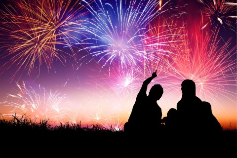 Two people silhouetted against a sky full of colourful fireworks.
