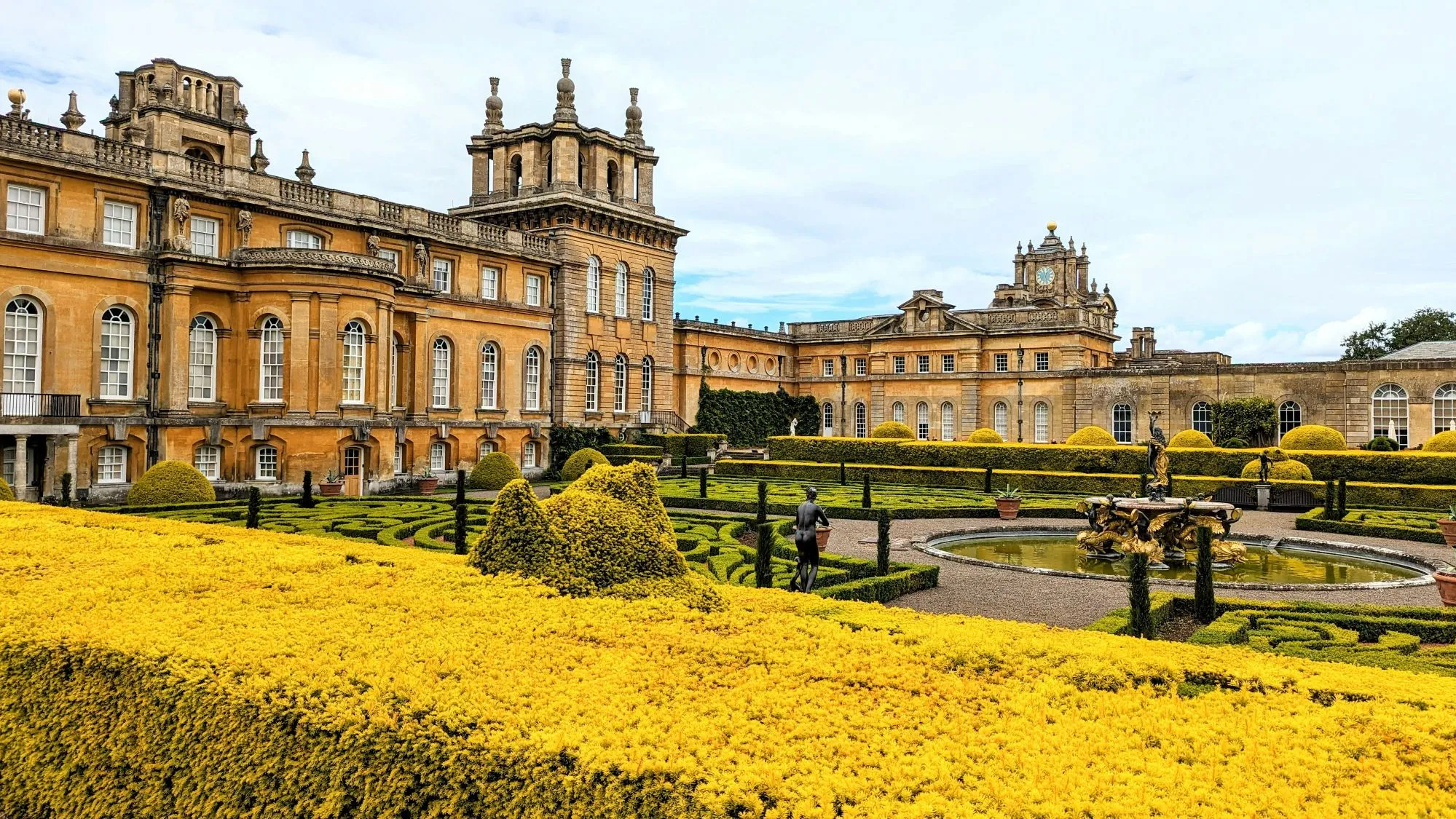 Exterior view of Blenheim Palace and its surrounding gardens under a clear sky.