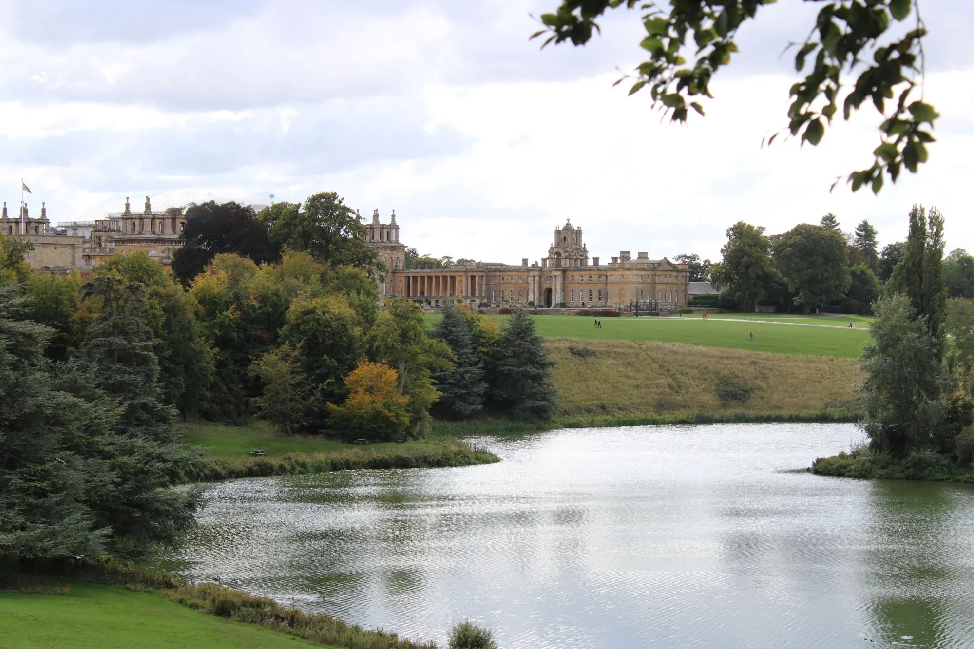 View of Blenheim Palace set behind a calm lake and an expansive green lawn.