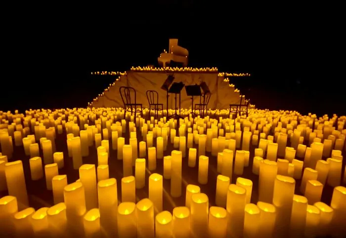 A floor full of candles with a grand piano, chairs, and music stands amongst them.