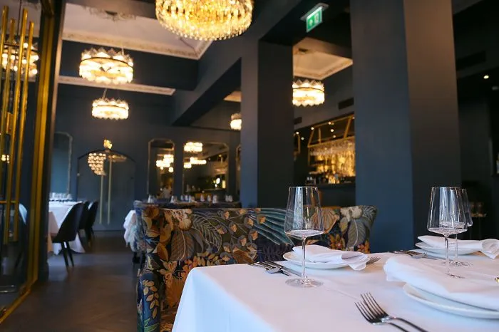 A classy restaurant with blue paint on the walls, decorative seating, and a laid table.