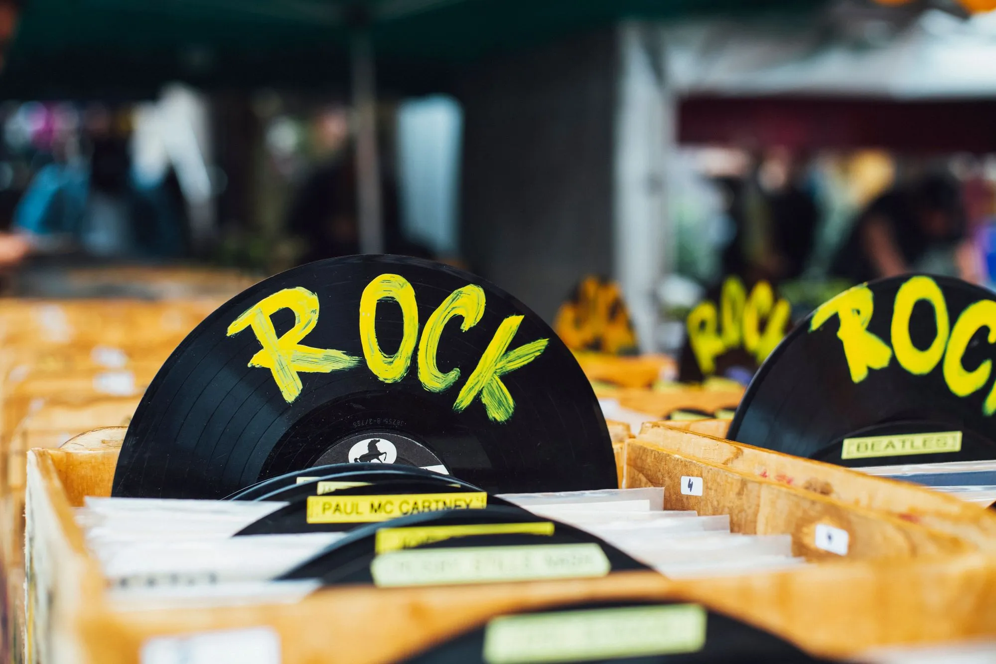 Rows of vinyl records in a record store with wooden divider tabs labelled with artists like The Doors, Eagles, and Hendrix.