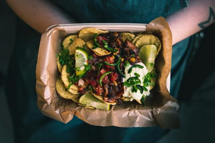  A person holding a takeaway tray filled with chips, salsa, lime, and more.