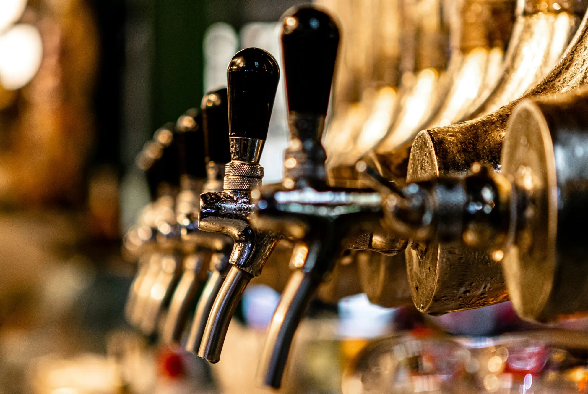 A close-up row of metallic draft beer taps with black handles at a dimly lit bar.