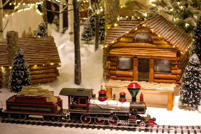 A toy train on tracks next to a miniature log cabin.